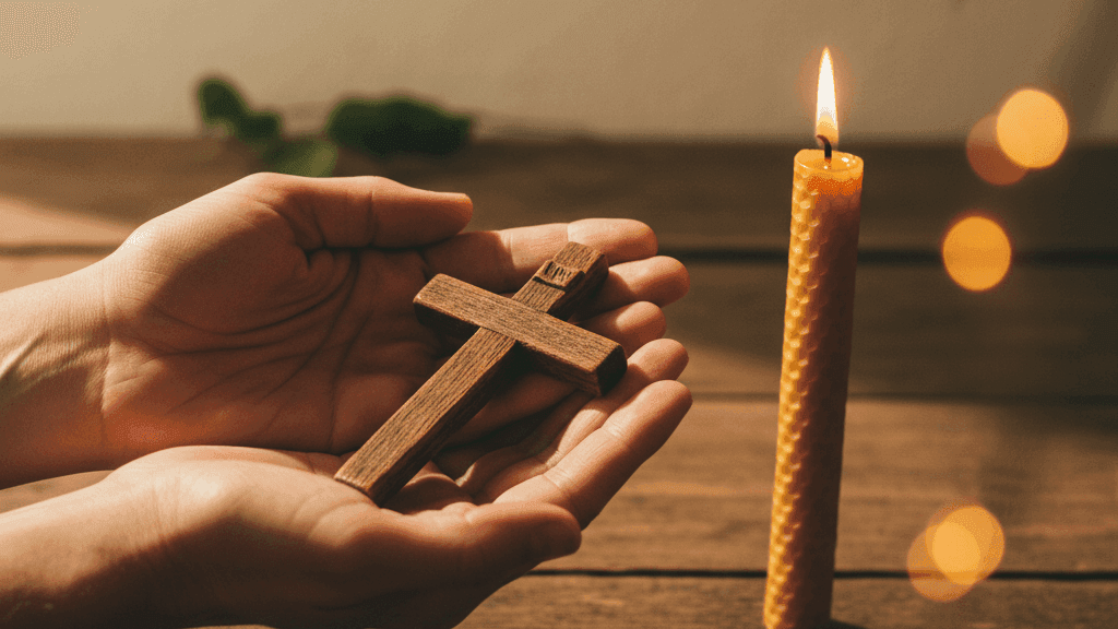 A small wooden crucifix resting in open hands beside a lit beeswax candle, warm amber light casting soft shadows across a simple wooden table — a visual of surrender to Christ in prayer